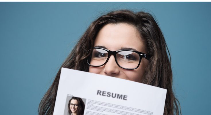 A woman holding up her resume such that it covers her lips but not her nose.