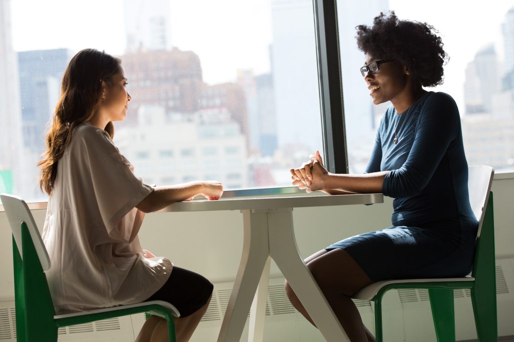 Two people mid interview at a round table sitting on wooden chairs